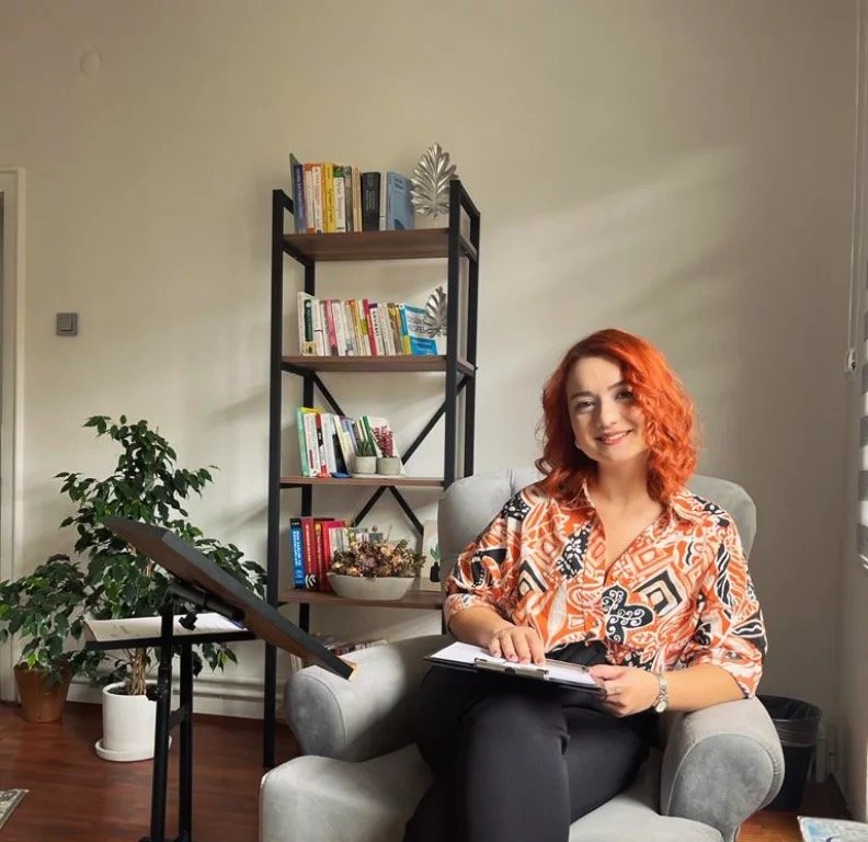 Uzm. Psk. Elif Çetinkaya, Ankara Tunalı'daki terapi ofisinde koltukta otururken gülümsüyor